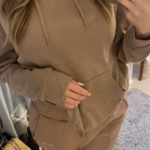 Beige-brunt Mjukisset - Mysig beige-brun hoodie från Primark med huva och känguruficka framtill. Tröjan har långa ärmar och en relaxed passform, perfekt för chill dagar. Mysiga beige-bruna byxor med Scrunch i slutet av benen och midjan. Byxorna har snören så man kan knyta och välja midjemått, från NAKD. Tillverkad i mjuk bomullsmix som känns skön mot huden.