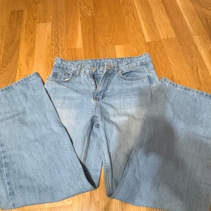 Ljusblåa wide jeans med rak passform - Säljer ett par ljusblå jeans med breda ben och rak passform. Klassisk femficksmodell i mjukt denimtyg, perfekt för dig som gillar en avslappnad och trendig stil. Passar till sneakers eller boots och är riktigt snygga till en enkel t-shirt. Har dock en liten fläck 