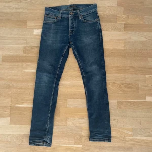 Mörkblå jeans från Nudie Jeans - Snygga mörkblå jeans från Nudie Jeans med klassisk femficksdesign och kontrastsömmar. Jeansen har en rak passform och är tillverkade i slitstarkt denimtyg av bomull. Perfekta för dig som gillar stilrena och tidlösa jeans med en cool tvätt.