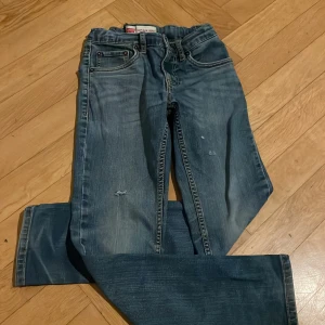 Levi's 512 Slim Taper jeans blå - Säljer ett par Levi's 512 Slim Taper jeans i klassisk blå tvätt. Jeansen har fem fickor, smal passform och avsmalnande ben. Snygga slitningar och detaljer som ger en cool, använd look. Perfekta för dig som gillar en modern och stilren jeansstil.