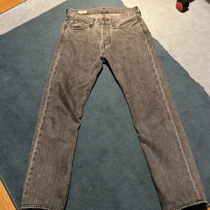 Levi's 501 grå jeans - Säljer ett par klassiska Levi's 501 jeans i grå tvätt. Är w 28 L32 men ör upp syda så skulle säga L30. De har rak passform, Jeansen är tillverkade i slitstarkt denim och har den ikoniska läderpatchen bak i midjan. Perfekta för en avslappnad och tidlös stil.