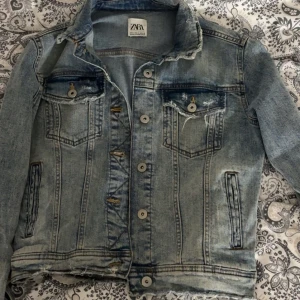 Ljusblå jeansjacka från Zara - Snygg ljusblå jeansjacka från Zara i klassisk modell med slitna detaljer och knappar framtill. Jackan har två bröstfickor med lock och knapp samt två sidofickor. Perfekt att slänga över en t-shirt för en chill look.
