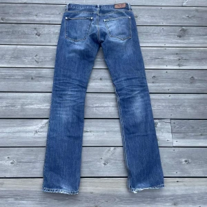 Blå raka jeans från Acne - Säljer ett par klassiska blå jeans från Acne med raka ben och snyggt slitna detaljer. Jeansen har fem fickor, normal midja och är tillverkade i robust denim. Perfekta för dig som gillar en tidlös och avslappnad look. Helt oanvända, gylfen är trasig, men annars inga defekter.