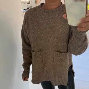 Brun stickad tröja med fickor - Mysig brun stickad tröja med två stora fickor framtill och ribbade muddar vid ärmslut och nederkant. Tröjan har en loose passform och lång ärm, perfekt för att chilla eller hänga med vänner. Rund hals och diskreta slitsar på sidorna ger extra stilpoäng.