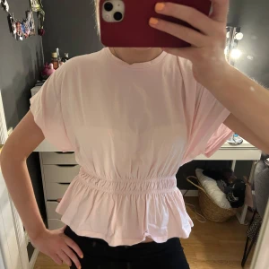 Ljusrosa blus med resår - Supersöt ljusrosa blus från 157 med korta ärmar och rund hals. Toppen har resår i midjan som ger en snygg volangkant och markerad siluett. Perfekt för dig som gillar en feminin och chill stil. Toppen är helt oanvänd men har tagit bort prislapparna🌸🌸