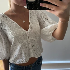 Vit broderad blus från H&M - Superfin vit blus från H&M med broderade blommor och v-ringning. Blusen har puffiga trekvartsärmar och knappar framtill.