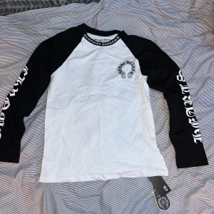 Chrome Hearts svartvit långärmad tröja - Snygg långärmad tröja från Chrome Hearts i svart och vitt. Tröjan har svartvita kontrastärmar med tryckt logga längs båda ärmarna och Chrome Hearts-tryck på bröstet. Crewneck med tryckt text runt halsen. Tillverkad i mjuk bomull. 0bs lnte 0rglnal 