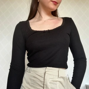 Långärmad tröja med spets - Svart topp med långa ärmar och ribbad struktur. Fyrkantig ringning med spetskant och liten rosett framtill.🥰Från H&M Divided!