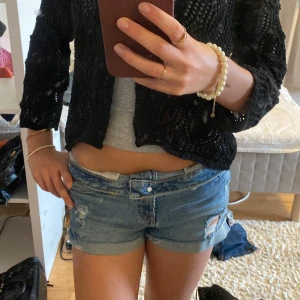 Lågmidjade jeansshorts från Zara - Säljer ett par blå denimshorts från Zara Trafaluc med låg midja och rullade benslut. Shortsen har slitna detaljer och en klassisk femficksmodell. Perfekta för varma dagar och en avslappnad look.