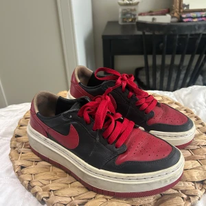 Nike Air Jordan elevated Low svart/röd - Snygga Nike Air Jordan 1 Low sneakers i svart och rött skinn med klassisk vit sula och röda snören. Ikonisk design med perforerad tå och lågt skaft, perfekt för dig som gillar streetstyle och vill sticka ut. Nike Air-logga på innersulan och tydlig swoosh på sidan. Detta är den ”elevated” designen. Storlek 36.5 passar 37 - är själv 37.