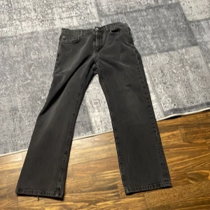 Svarta jeans från Woodbird - Snygga svarta jeans från Woodbird med en straight passform. De har en klassisk design med fem fickor och en dragkedja. Byxorna har en fransig detalj vid bensluten som ger en cool touch. Skick 6/10