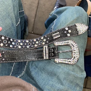 Svart glittrigt bälte från B.B. Simon - Snyggt äkta svart bälte från B.B. Simon med glittriga stenar. Bältet har en stor, dekorerad spänne och är perfekt för att ge en extra touch till din outfit. Bältet är 117cm långt! Hör gärna av er vid fler frågor eller funderingar😇                                  MVH Timmi