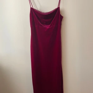 Vinröd sammet klänning - Elegant vinröd klänning i mjuk sammet med smala axelband och en subtil spetsdetalj vid halsringningen. Perfekt för en stilfull kväll. Färgen varierar lite beroende på ljus, kan dra sig mer vinrött, rosa eller lila. Ser lite mer lila ut i verkligheterna jämfört med bilderna.   Passform: Längden går till några centimeter under knäna på mig som är 172cm lång.  Stretchigt material förutom under delen vid bysten som är mer av ett silkes material, ungefär som en inbyggd bh.