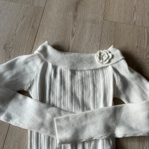 Vit ribbad of shoulder tröja från SHEIN - Säljer en stilren vit of shoulder ribbad tröja från SHEIN med en söt blomdetalj vid halsen. Tröjan har långa ärmar och en bred krage som ger en elegant touch.🩷🩷
