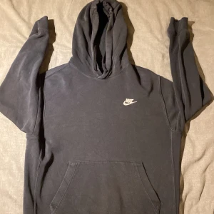 Svart hoodie från Nike - Säljer en klassisk svart hoodie från Nike med vit logga på bröstet. Tröjan har en stor ficka framtill och en bekväm huva med dragsko. Perfekt för en avslappnad stil. Kan gå ner i pris vid snabb affär