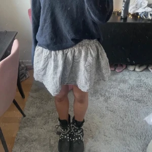 Rutig kortkjol - Säljer en söt rutig kortkjol i svart och vit. Kjolen har en volangdetalj och en elastisk midja för en bekväm passform.