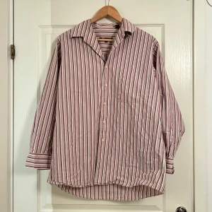 Randig skjorta med långa ärmar - Säljer en stilren randig skjorta med långa ärmar. Skjortan har en klassisk krage och knäppning framtill. Perfekt för en avslappnad men ändå uppklädd look.