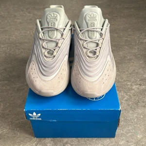 Grå Adidas Ozelia  - Snygga grå sneakers från Adidas med en futuristisk design och vågformade detaljer. Skorna har en rund tå och snörning för en säker passform. Perfekta för en clean look