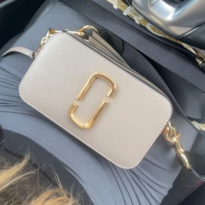 Marc Jacobs väska - Snygg axelväska i beige och brun med gulddetaljer. Väskan har en justerbar axelrem med mönster och en dragkedja upptill. Marc Jacobs väska. Fint skick. 