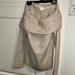 Beige stickad offshoulder-tröja - Säljer en mysig beige stickad tröja med offshoulder-design. Tröjan har en bred ribbad krage och långa ärmar, perfekt för kyliga dagar. Den är både stilren och bekväm, ett måste i garderoben! Aldrig använd💗