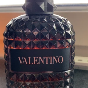 Valentino coral fantasy - Elegant parfymflaska från Valentino med en lyxig design i mörkt glas och ett mönster av små pyramider. Flaskan har en svart etikett med märkesnamnet i en ljus rosa färg. Perfekt för den som söker en sofistikerad doftupplevelse.