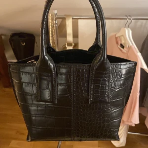 Liten svart handväska  - Snygg svart handväska. Väskan har både handtag och en guldig kedja som axelrem för flexibilitet.