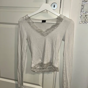  långärmad topp med spetsdetaljer - Säljer en stilren vit långärmad topp från Gina Tricot med v-ringning och spetsdetaljer vid hals och nederkant. Perfekt för en elegant look!💗