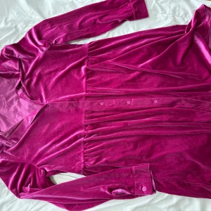 Mörkrosa sammetklänning - Säljer en elegant mörkrosa klänning i mjuk sammet med långa ärmar och knappar framtill. Perfekt för en stilfull look.