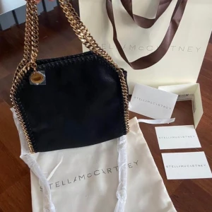 Svart Stella McCartney väska med guld kedjor - Säljer min älskade Stella väska! Köpt på Stella McCartneys butik i London i somras förra året 💝 super fint skick, inga defekter överhuvudtaget. Jag har varit väldigt försiktig med väskan 💕köpt för 9900kr (775£). Det är modellen Tiny Falabella. Skriv innan ni köper 🥰🥰