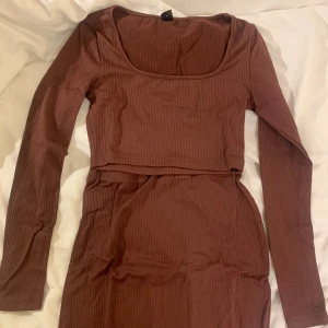 Matchande sett topp och kjol - Säljer en snygg brun topp med matchande kjol som har slits. Settet har en figurnära passform och är gjord i ett mjukt material.