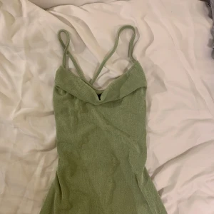 Grön klänning med snörning - Snygg grön klänning med smala axelband och en stilren design. Klänningen har en öppen rygg med dekorativ snörning som ger en unik touch. Perfekt för sommaren. 