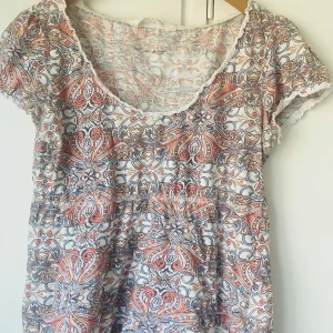 Mönstrad blus från Odd Molly - Säljer en färgglad blus från Odd Molly med ett intrikat mönster i orange, blått och vitt. Blusen har korta ärmar och en v-ringad halslinje med spetsdetaljer. Perfekt för en bohemisk look!