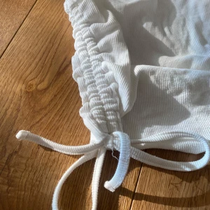 Vit ribbad linnetopp - Säljer en stilren vit ribbad linnetopp med knytband i sidorna. Perfekt för varma dagar och kan enkelt matchas med olika outfits. Toppen har en klassisk rund halsringning och ärmlös design.