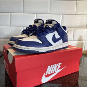 Nike Dunk i blått och vitt - Snygga Nike Dunk sneakers i en fräsch kombination av blått och vitt. Skorna har en klassisk design med snörning och rund tå, perfekt för en stilren look. De kommer i originalkartong och är redo att bäras till både vardag och speciella tillfällen. Kom priv för frågor eller minsta lilla fundering 