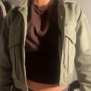 Grön croppad jacka - Säljer en snygg grön croppad jacka med långa ärmar och knappar framtill. Jackan har en cool och avslappnad stil, perfekt för att lyfta din outfit. Den har en klassisk krage och praktiska fickor på bröstet.