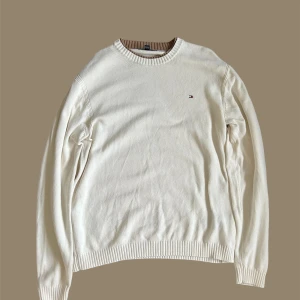 Vit tröja från Tommy Hilfiger - Säljer en stilren vit tröja från Tommy Hilfiger med deras ikoniska logga broderad på bröstet. Tröjan har långa ärmar och ribbade muddar vid ärmslut och nederkant. Perfekt för en klassisk och avslappnad look.