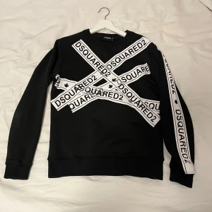 Dsquared2 tröja - Säljer en svart tröja från Dsquared2 med vita band och logotypen tryckt över bröstet och ena ärmen. Perfekt för en stilren och modern look.