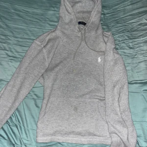 Grå hoodie från Ralph Lauren - Säljer en stilren grå hoodie från Ralph Lauren med klassisk passform. Tröjan har en känguruficka och en liten broderad logga på bröstet. Perfekt för en avslappnad look.