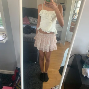 Rosa volangkjol - Söt rosa kortkjol med volanger och ett diskret mönster. Kjolen har en elastisk midja för en bekväm passform. Perfekt för varma dagar och ger en romantisk touch till din outfit.