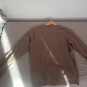 Beige långärmad tröja från Boss - Säljer en stilren beige långärmad tröja från Boss. Tröjan har en enkel design med en liten logotyp på bröstet. Perfekt för en avslappnad och elegant look.