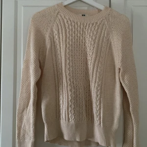 Beige stickad tröja från Uniqlo - Säljer en mysig beige stickad tröja från Uniqlo med flätstickat mönster. Tröjan har långa ärmar och ribbstickade muddar vid ärmslut och nederkant. Perfekt för kyliga dagar!