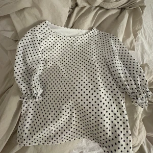 Vit prickig  blus med volang vid armarna  - Säljer en söt vit blus med svarta prickar. Blusen har trekvartsärmar med elastiska ärmslut som ger en fin puffeffekt. Köpte i Paris på secondhand så det står inget märke 💓