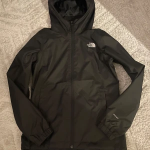  The North Face oanvänd - Säljer en svart vindjacka från The North Face med huva och dragkedja. Jackan har långa ärmar och är perfekt för blåsiga dagar. Den är stilren och funktionell med logotypen på bröstet och ryggen. ALDRIG ANVÄND 