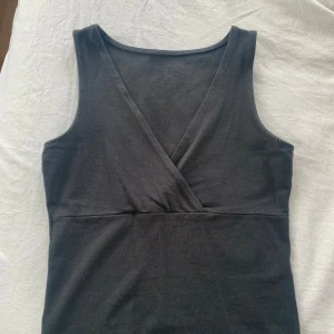 Svart omlott linnetopp - Säljer en svart ärmlös linnetopp från Brandy Melville med omlott-skärning framtill. Perfekt för en stilren och enkel look. Mjuk och bekväm, passar till många olika outfits.