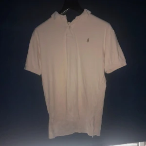 Vit piké från Polo Ralph Lauren - Säljer en klassisk vit pikétröja från Polo Ralph Lauren med broderad logga på bröstet. Tröjan har korta ärmar, krage och knappar vid halsen. Tillverkad i 100% bomull för en skön och luftig känsla.