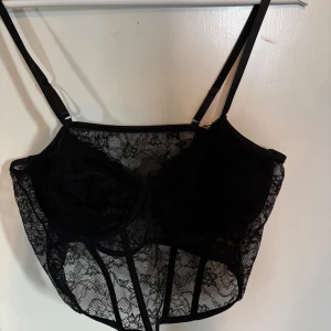 Svart spetskorsett från SHEIN - Säljer en svart korsettopp från SHEIN Curve i storlek 2XL. Toppen är gjord i genomskinlig spets med reglerbara axelband och markerade sömmar framtill. Perfekt för att skapa en edgy och trendig look.