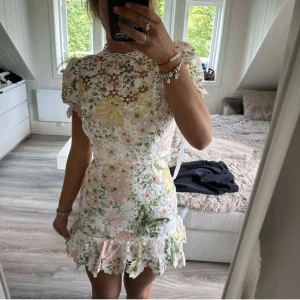 Blommig spetsklänning med volang - Säljer en söt kortklänning med blommigt mönster i pastellfärger. Klänningen har spetsdetaljer, volang nertill och korta ärmar. Perfekt för sommarens alla tillfällen!