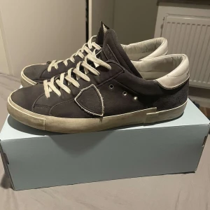 Philippe Model - Säljer ett par Philippe Model sneakers i mörkblå mocka med vita detaljer och snörning. Skorna har en vit platt sula och rund tå. Märkeslogga syns på hälen och sidan. Perfekta för en stilren och avslappnad look. Storlek 43 men passar även 44.