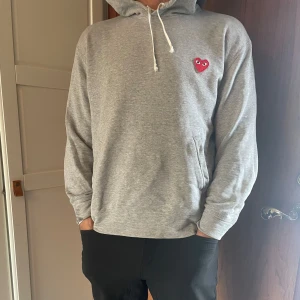 Grå hoodie med rött hjärta från Comme des Garçons Play - Säljer en grå hoodie från Comme des Garçons Play med det ikoniska röda hjärtat broderat på bröstet. Tröjan är storlek M men sitter som en L skulle jag säga. Hör av er vid frågor! 