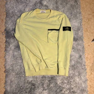 Ljusgul sweatshirt från Stone Island - Säljer en ljusgul sweatshirt från Stone Island med rund halsringning och en ficka med dragkedja på bröstet. Klassisk logotyp-patch på vänster ärm. Perfekt för dig som gillar streetwear och snygga detaljer.